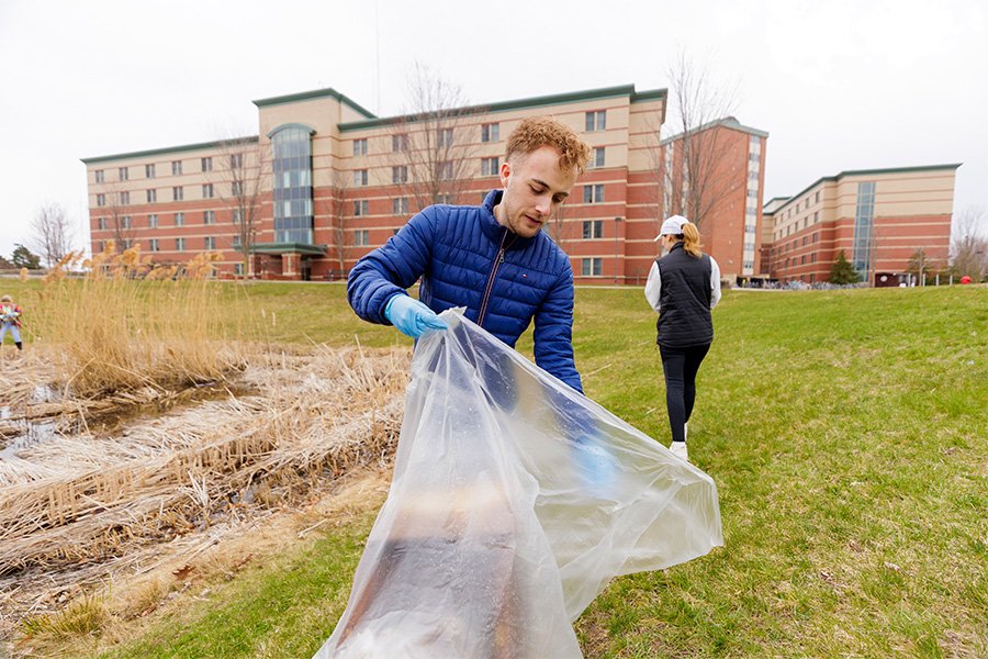 A student holds a trash bag outside. The student picks up litter and debris from campus.