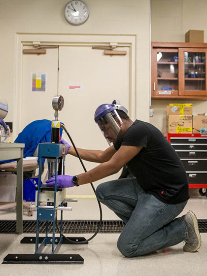 A student wearing a face shield and plastic gloves works in a physics lab on campus.