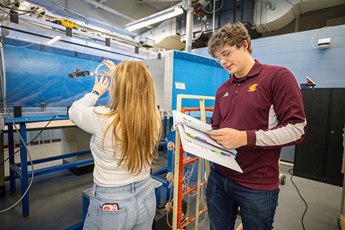 Two students conduct a wind tunnel experiment in a laboratory.