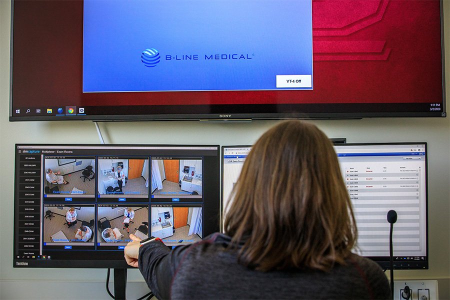 A woman looking at two computer screens and pointing to one of the video camera feeds.