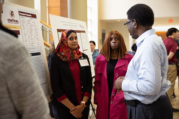 Three individuals talking next to a research poster at a conference.