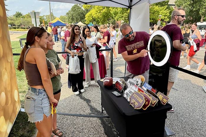 Two students pose in the photo booth while a staff member works the equipment.