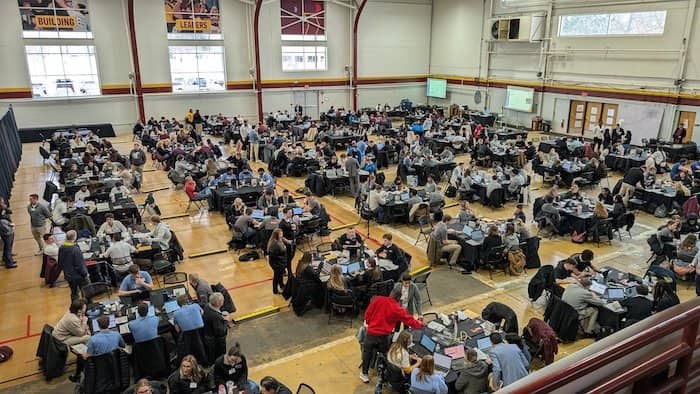 Photo of hundreds of students working on laptops at tables spread across a field house floor.