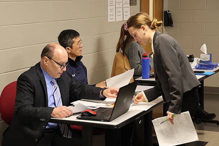 Teachers and CMU Faculty huddled around a laptop in the hallway of Grawn Hall.