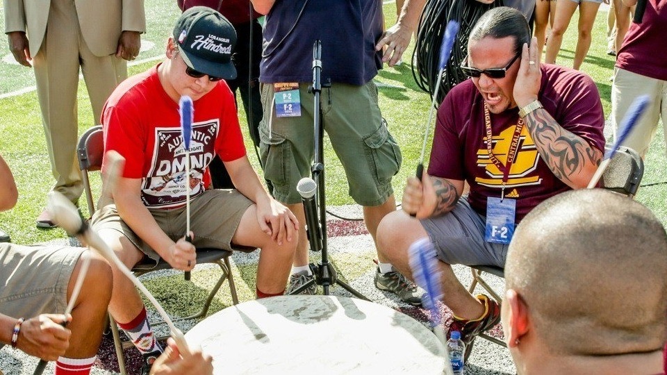 A group of people sitting in chairs with microphones in a drum circle.