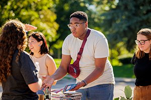 a group of people outside on a sunny day talking to each other while exchanging brochures