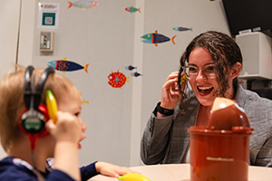 Blog CSD 2 A student wears headphones and works with a young boy who also has headphones on.