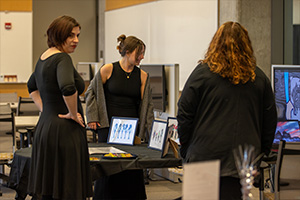 A group a three women in business attire gather around a computer screen preparing for a presentation.