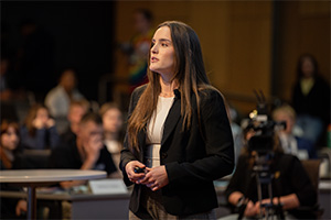 A woman in a business suit speaks to a crow of people in an auditorium.