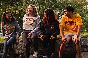 A group of students wearing Central Michigan University shirts and sweatshirts sits on a group of rocks outside the library.