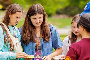A group of three young women and two adults talk about the information they're holding.