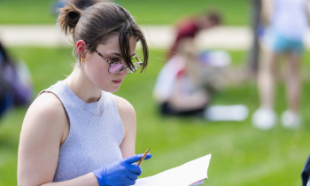 Forensics350x210 A student wearing blue latex gloves holding a pen and paper surveying a scene.