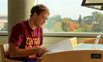 A student sitting at a library desk studying and reading a sheet of paper.