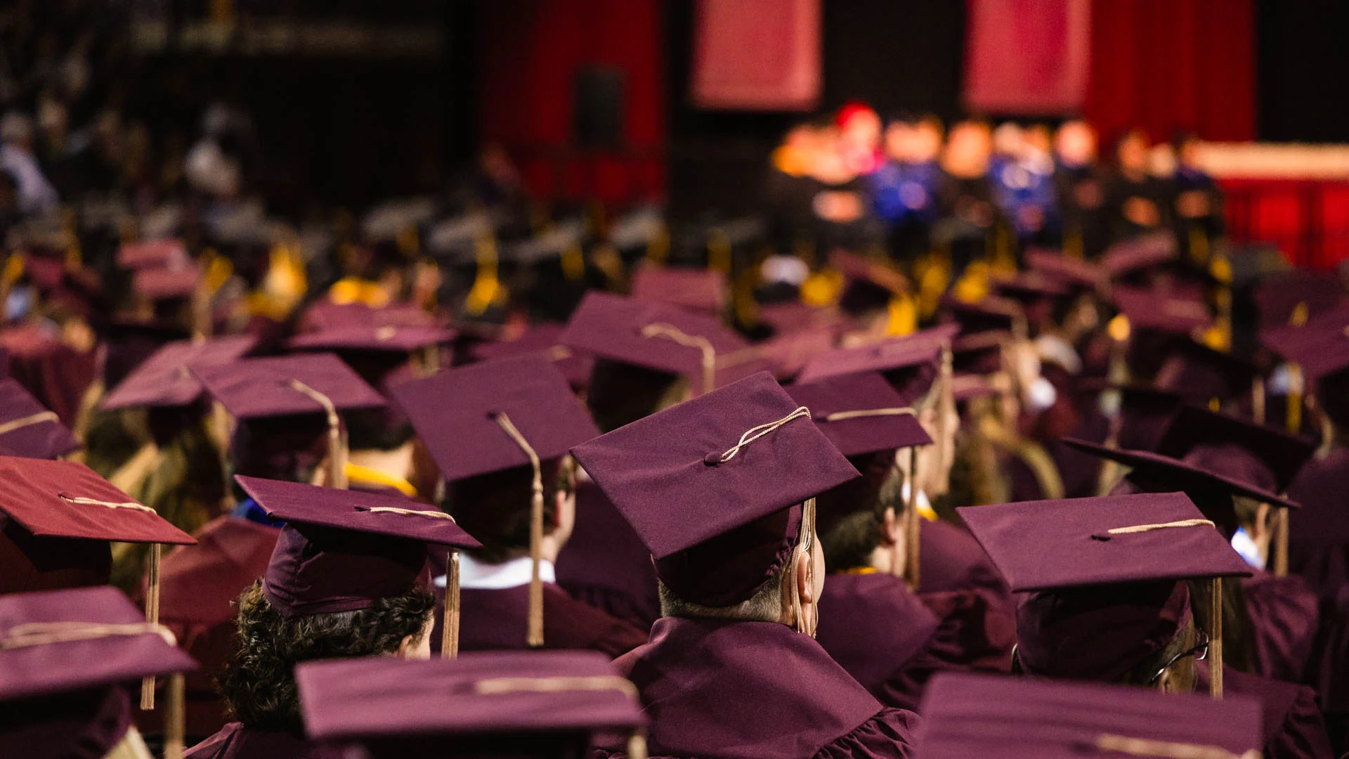a large crowd of graduates wearing maroon caps and gowns stand together at commencement ceremonies