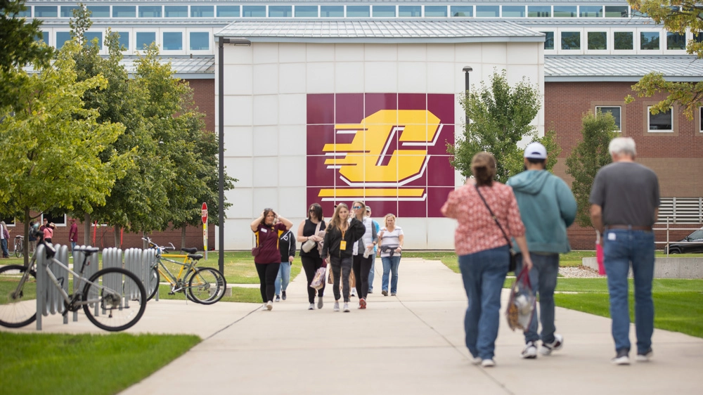 Two groups of people and a tour guide in maroon and gold walk outside for a CMU tour
