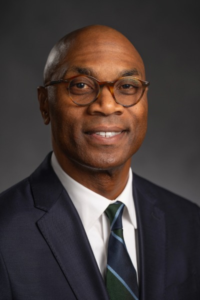 A man in a suit and tie smiling in a headshot photo.