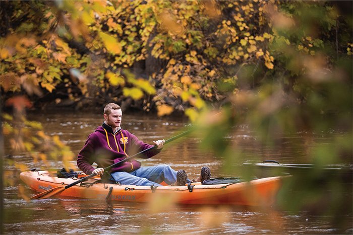 Young man in CMU jacket sits in a kayak on a river.