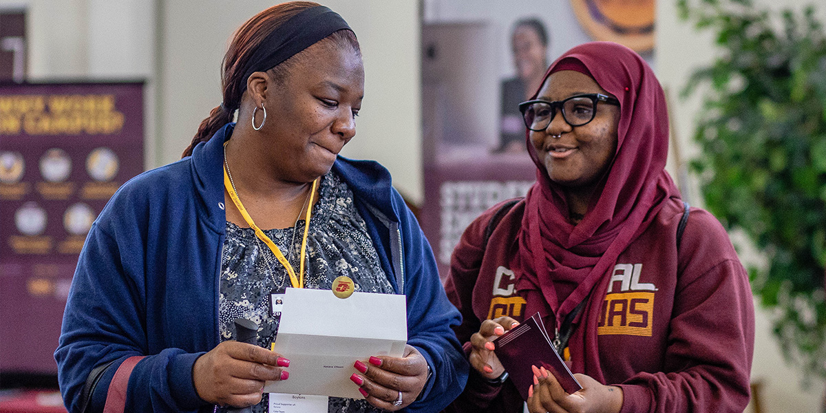 A student and their supporter stand smiling, holding a piece of paper.