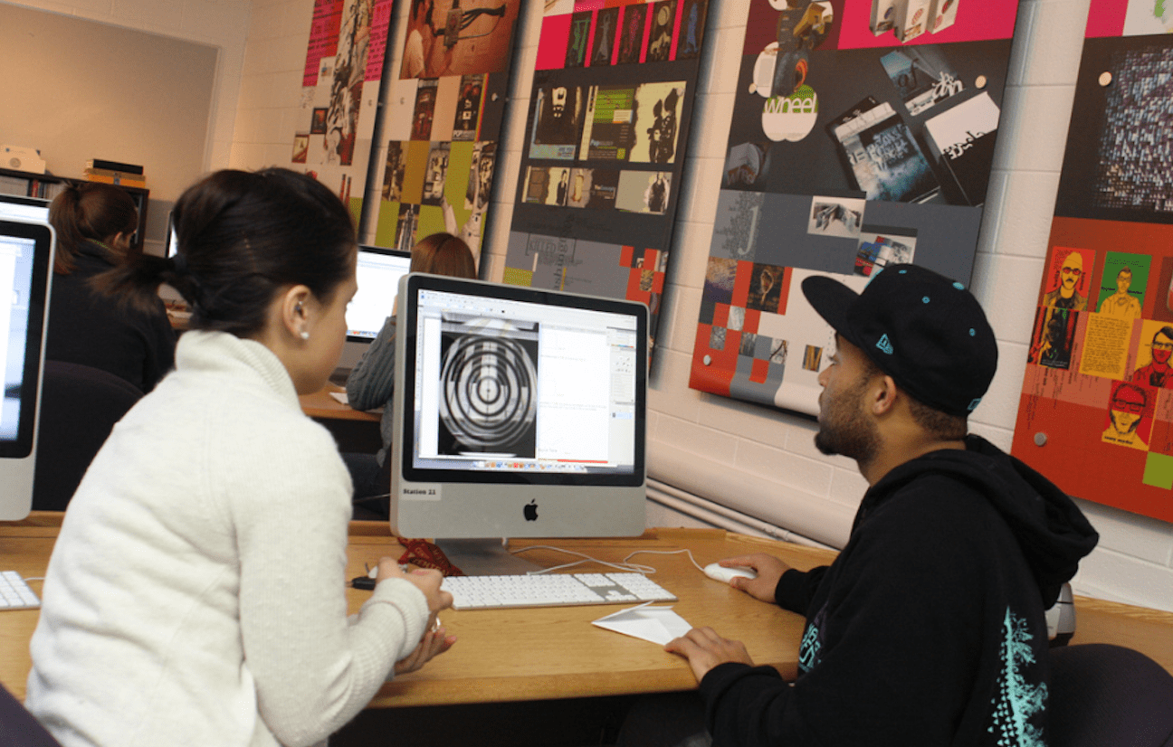 graphic-design-computer-lab Two students sitting in a computer lab while looking at a design on a computer screen.