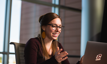 Student smiling and gesturing while attending a virtual class on a laptop with a CMU logo.