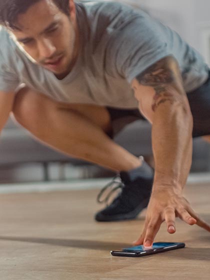 An athletic man with brown hair on his head and face and wearing workout clothing scrolls on his phone during a workout.