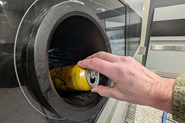 A hand guides an aluminum can into the opening of a bottle and can return machine.
