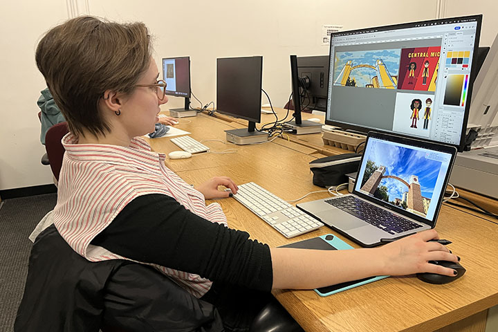 A woman wearing glasses manipulates a mouse with her right hand while looking at a computer monitor.