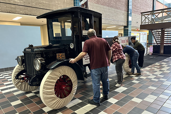 Four people prepare to roll an antique truck down the concourse of a building.