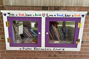 Two square purple doors inside a white frame with the words Take a book, leave a book, Love a book, keep a book written above them and Pullen Elementary School written underneath.