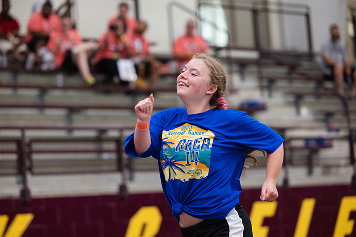 A female Special Olympics Michigan athlete sprints down an indoor track.