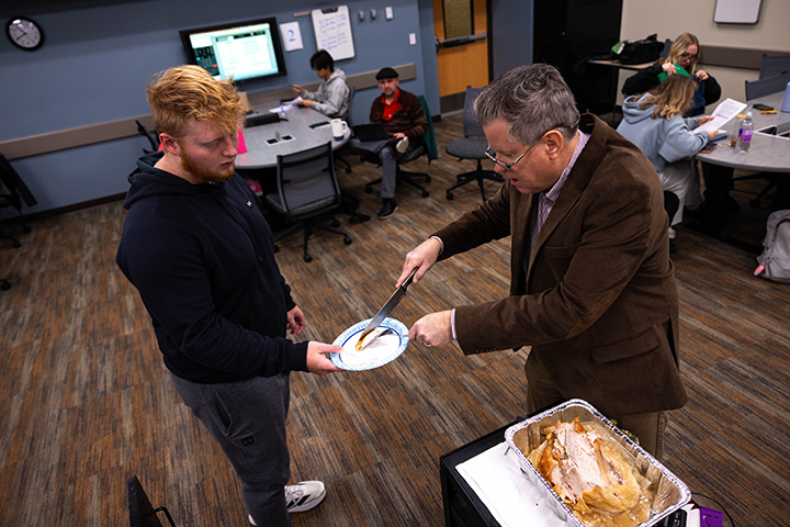 A faculty serves turkey to a student inside a classroom.