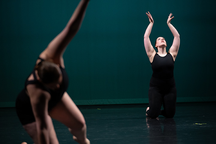Two women in black outfits dance on a stage