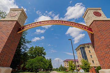 A sign over a brick archway on a sunny day.