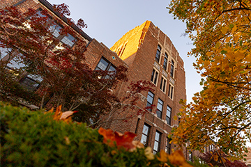 A tall brick building with trees and falling leaves.