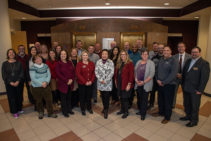 A group of people in business casual dress stand pose for a group photo in a building lobby