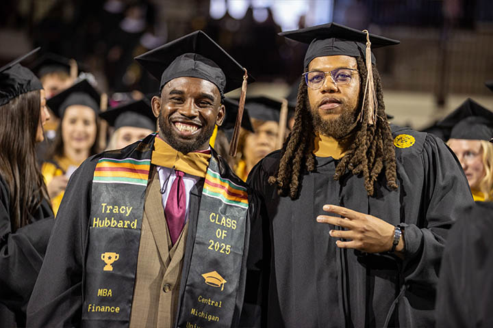 Two men smiling and wearing black graduation caps and gowns.