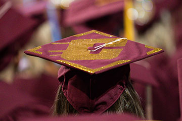 A student wears a maroon graduation mortarboard cap emblazoned with the CMU Action C in hold paint