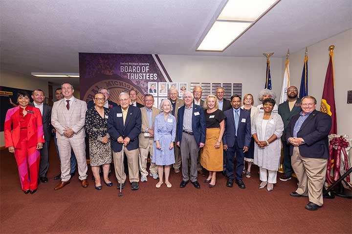 A large group of people wearing professional clothing stand in a line in front of a mural