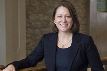A woman in a dark blazer smiles at the camera.