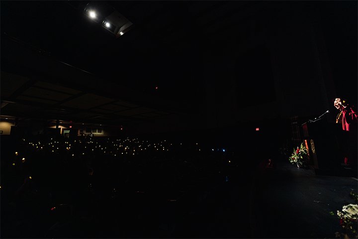 a man in a robe on stage holding up a candle with audience