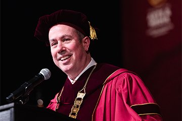 A man in red ceremonial regalia speaks into a microphone.