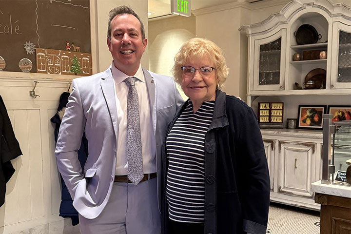 A man in a blue suit stands with a shorter woman in a black sweater .