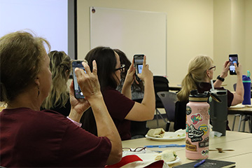 A group of people taking using their phones to take a picture in a classroom.