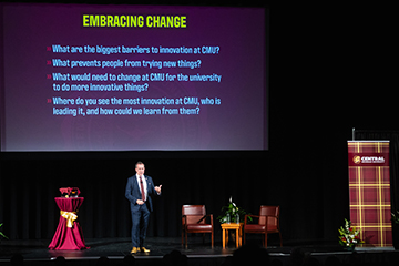 A man standing on a stage under a large screen.