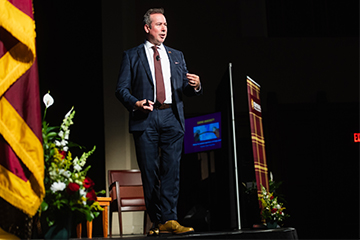 A man in a suit and tie speaking on a stage.