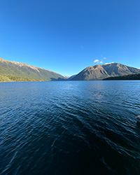 Blue lake water ripples in the foreground with hills in the background under a clear, blue sky.