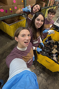 Four smiling young people wearing maroon shirts post in between two yellow bins full of socks