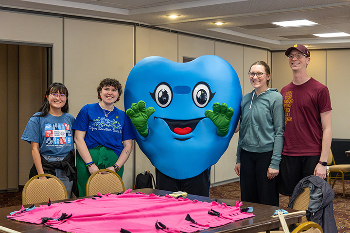 Four people pose for a photo with a blue-colored heart mascot