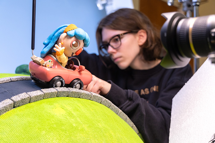 A student works on a stop motion film, adjusting a clay figure in a vehicle