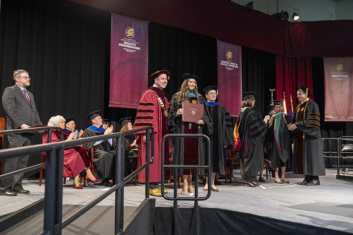 A doctoral graduate holds her diploma on stage at commencement